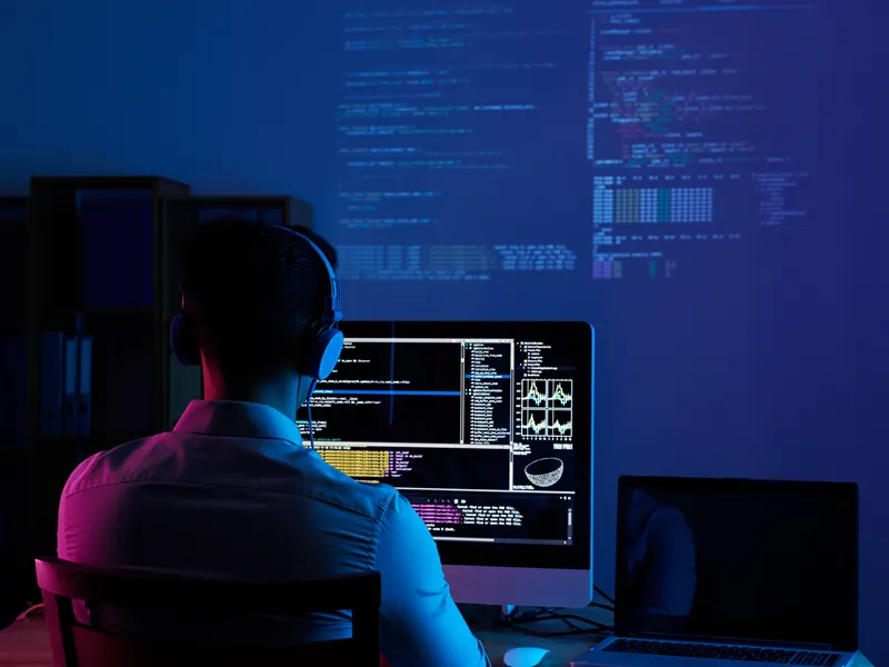 What makes DESSS a practical AI consulting company – Artificial Intelligence Consulting What makes DESSS a practical AI consulting company – Artificial: programmer working at multiple screens in a dark office